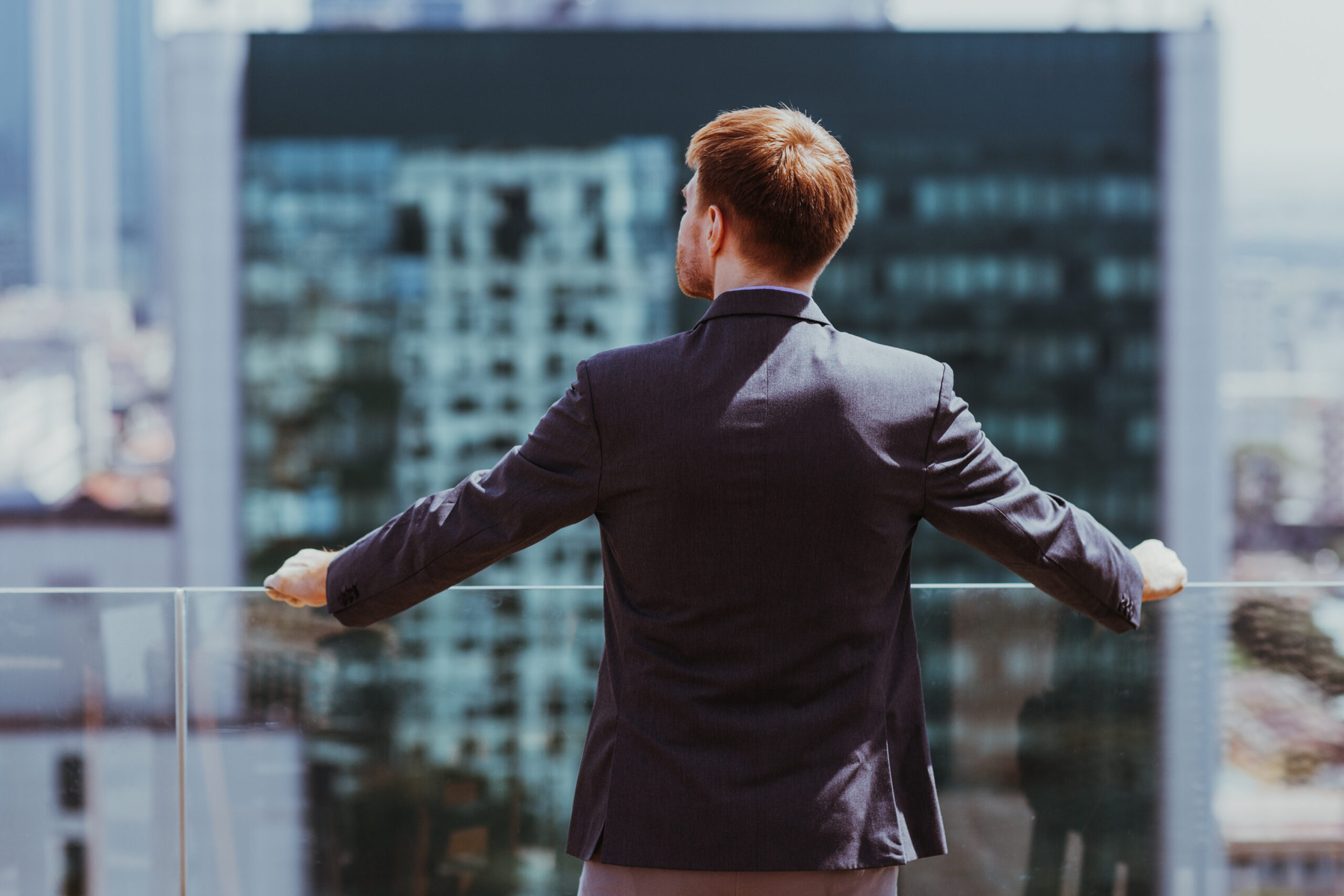 Portrait of successful businessman standing on balcony and looking at city view