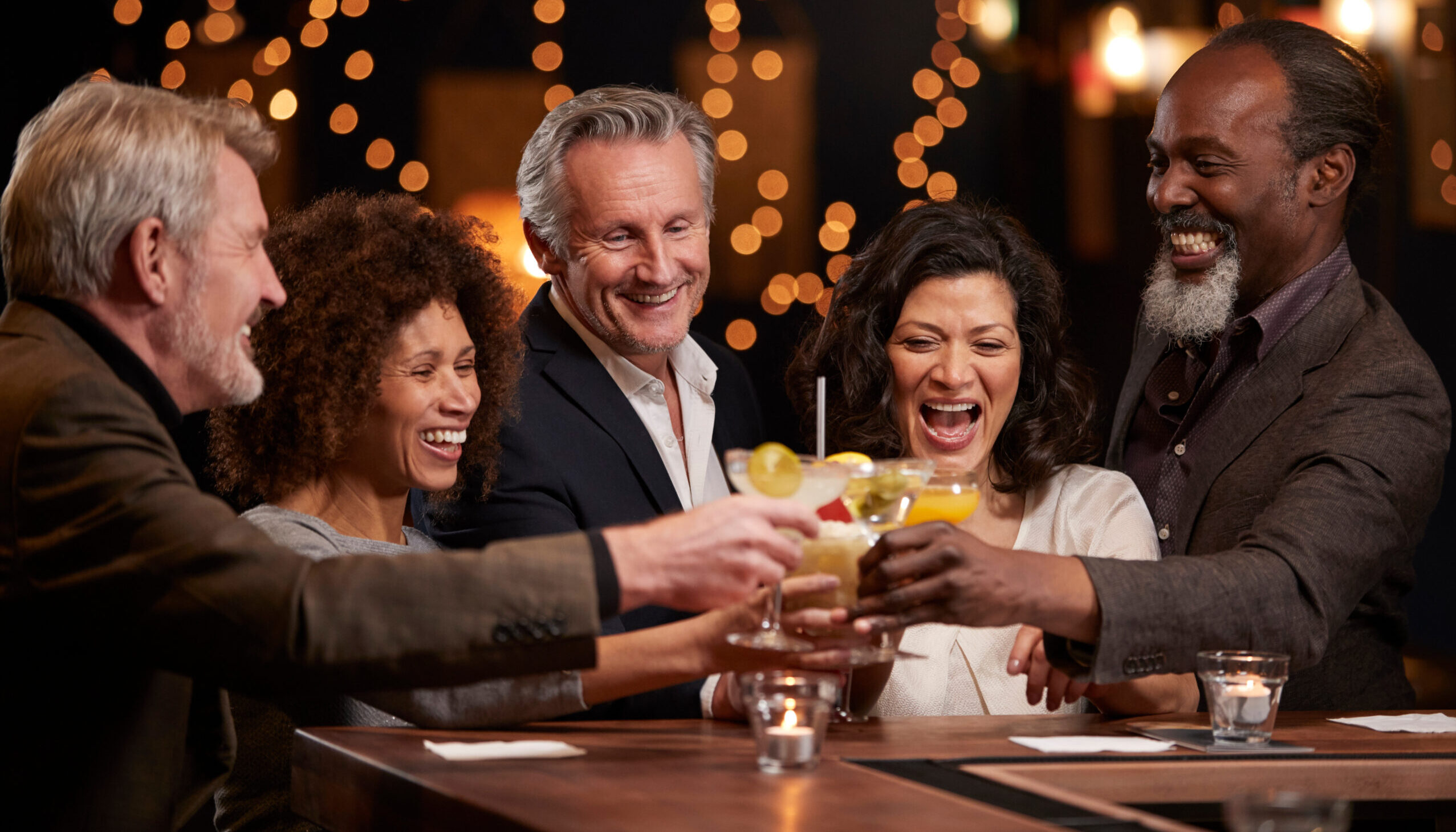 Group Of Middle Aged Friends Celebrating In Bar Together, cheers with cocktails, diversity