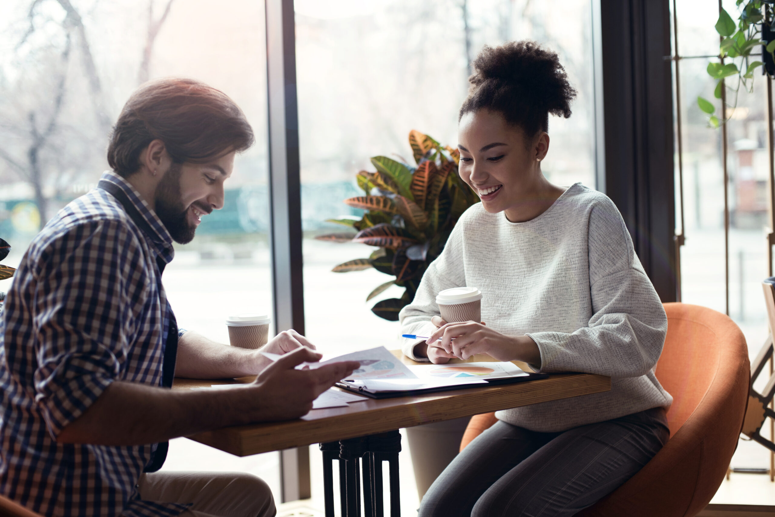 Young people man and woman coworking together at creative stylish office sitting at the table discussing new project smiling excited looking at documents