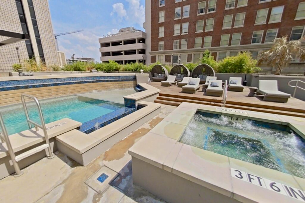 Pool area with hot tub, city view, lounge chairs, and covered couches