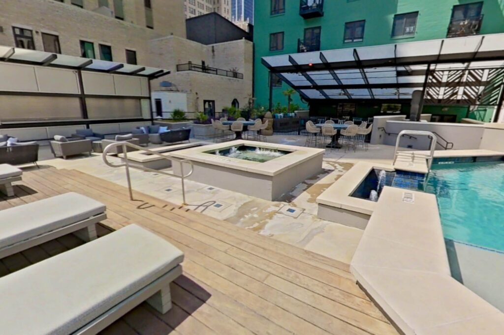 Poolside area with hot tub, covered seating, and lots of chairs, stools, loungers, and tables.