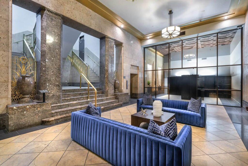 Hallway with grand stairway and two big blue couches leading into a mailroom