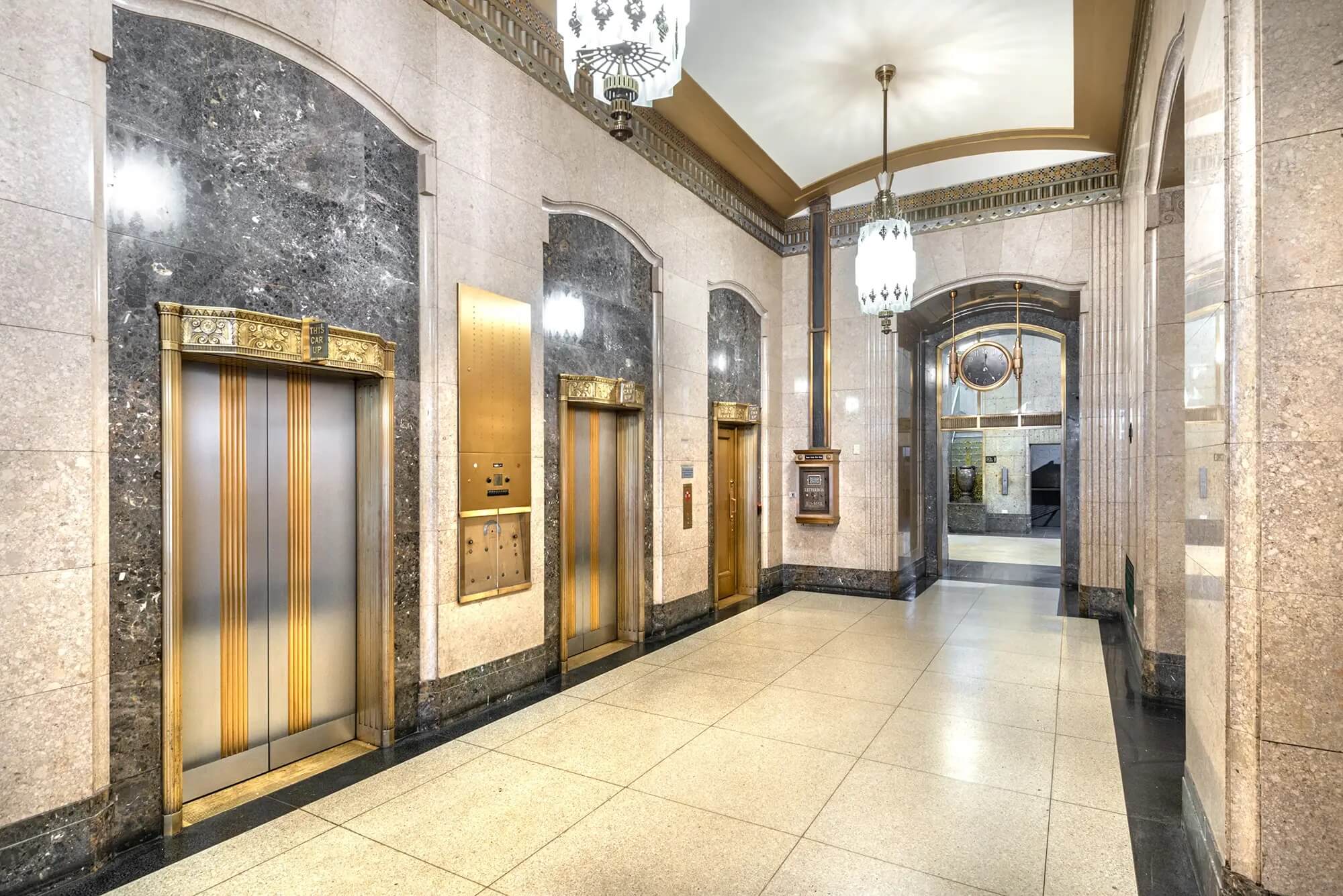 A grand hallway with gold lined elevators, very vintage margle and gold retro look