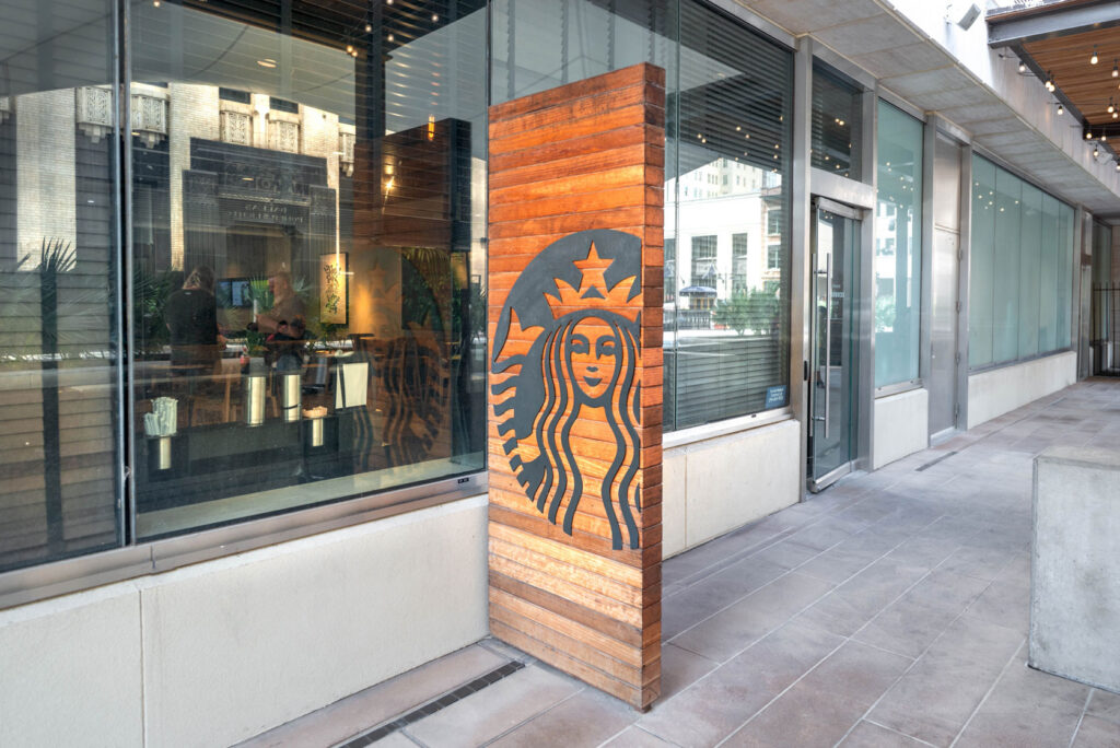 A Starbucks logo on a vertical wooden slat wall outside a glass-fronted storefront.