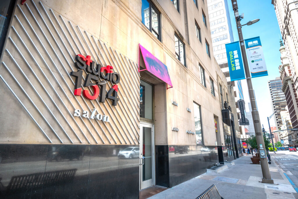 The exterior of Studio 1514 salon on a city street, featuring a large logo with red lettering and silver diagonal bars on the stone facade.