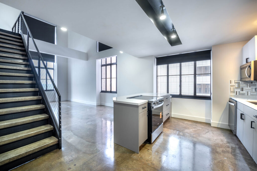 Modern loft apartment with a metal staircase, concrete floors, and a kitchen island.