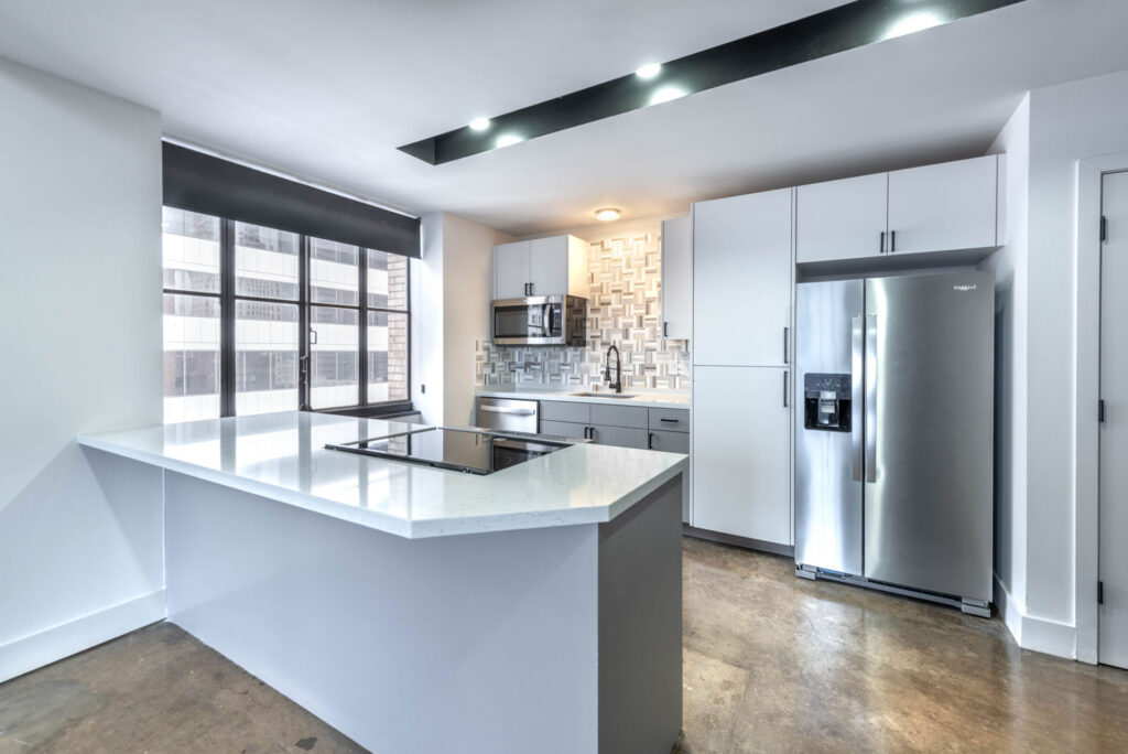 Modern kitchen with a gray island, white cabinetry, stainless steel appliances, and large windows.