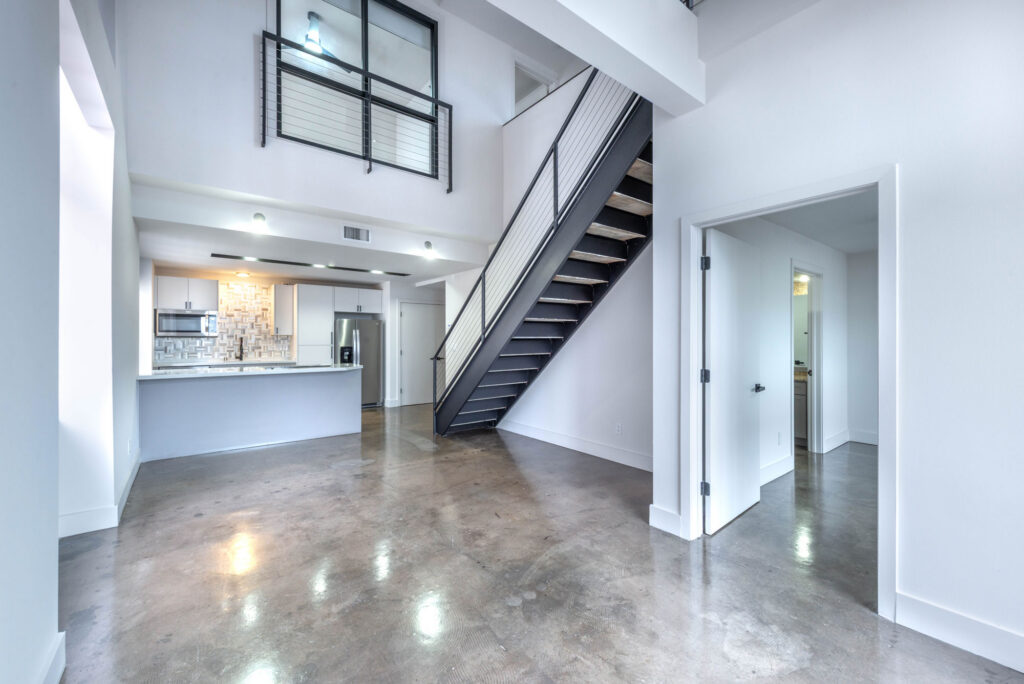 Modern apartment interior featuring an open kitchen, concrete floors, and a metal staircase leading to a loft.