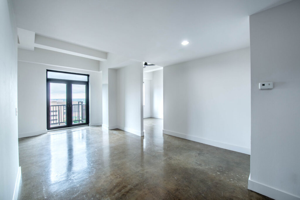 Empty room with white walls, a concrete floor, and glass patio doors leading to a balcony.