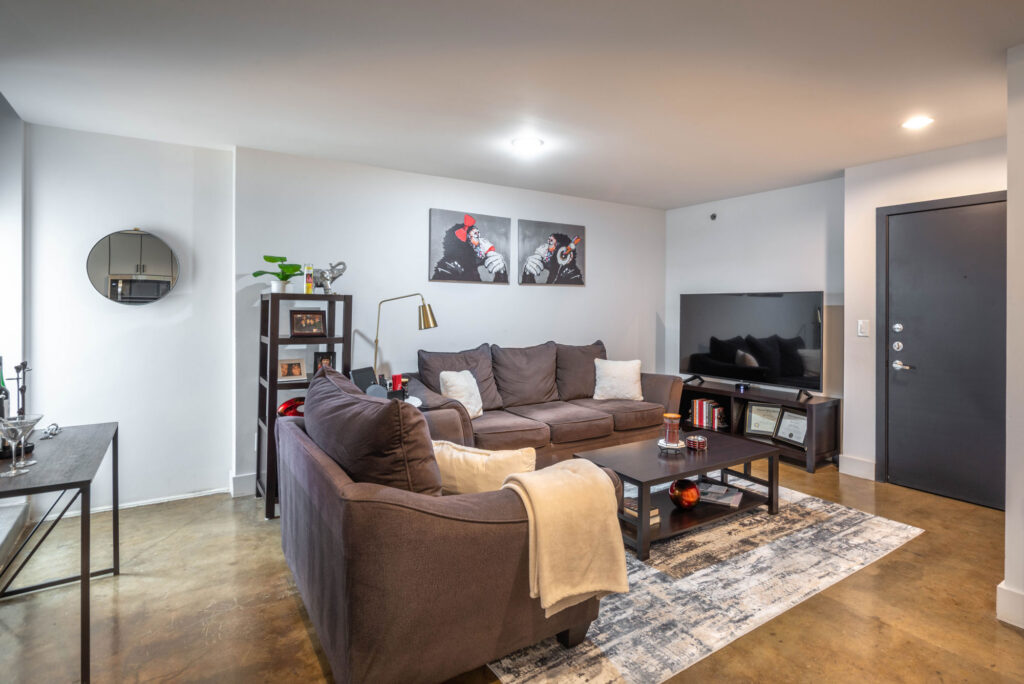 A living room featuring dark gray sofas, a coffee table, a television on a console, and two wall prints depicting a gorilla.