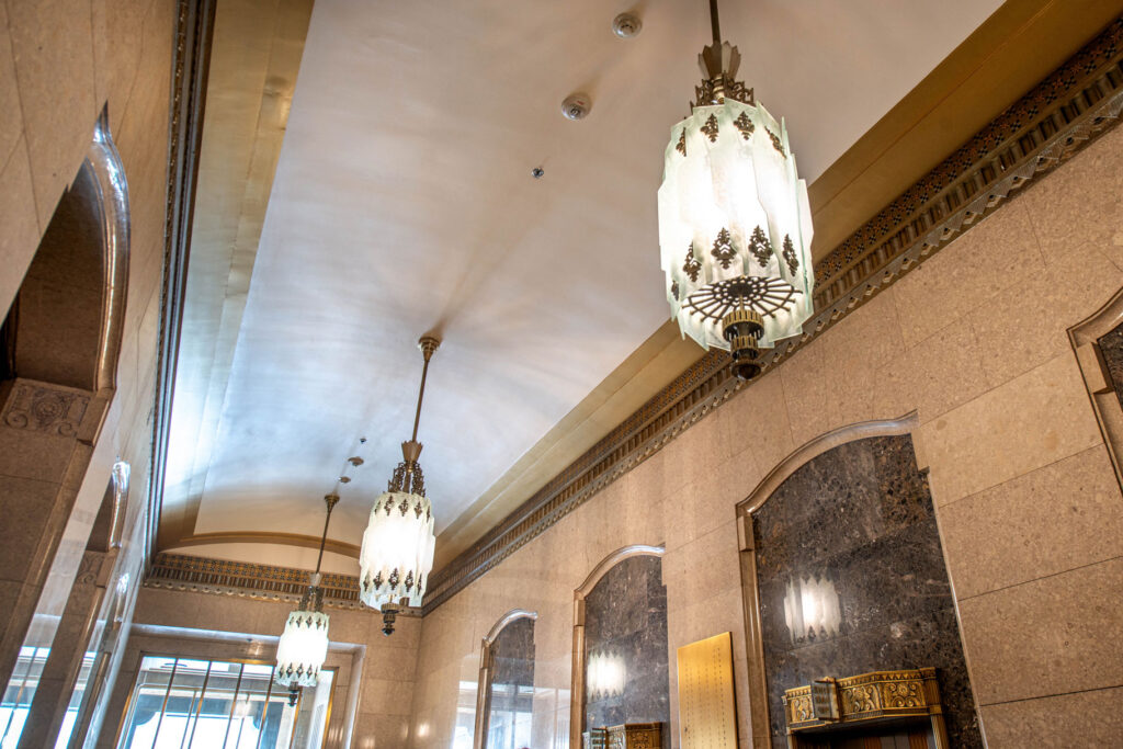A hallway with three ornate Art Deco-style hanging light fixtures and dark marble wall panels.