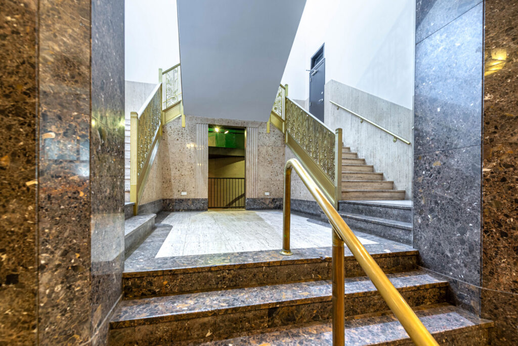 Grand indoor staircase with marble steps, gold railings, and decorative metal balustrades in a building foyer.