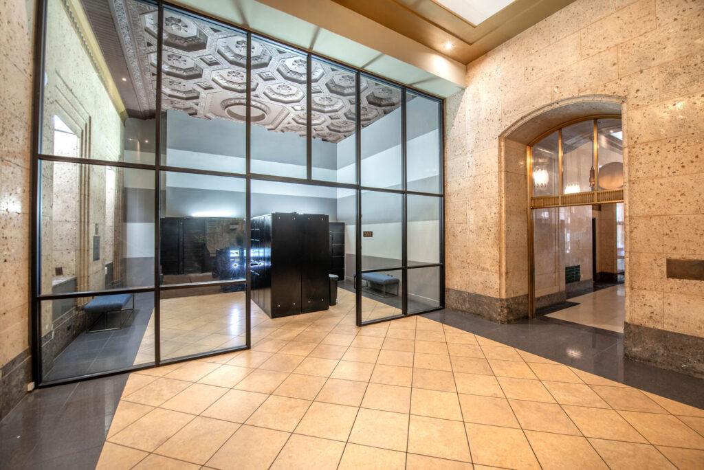 A glass-walled office partitioned from a lobby with stone walls and a geometric coffered ceiling.