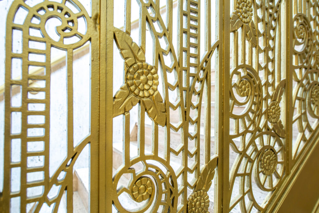 Intricate gold-painted metal railing with floral and geometric patterns lining a staircase.