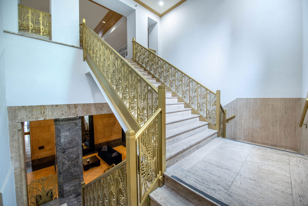 A grand staircase with ornate gold railings leads upward between light-colored stone walls.