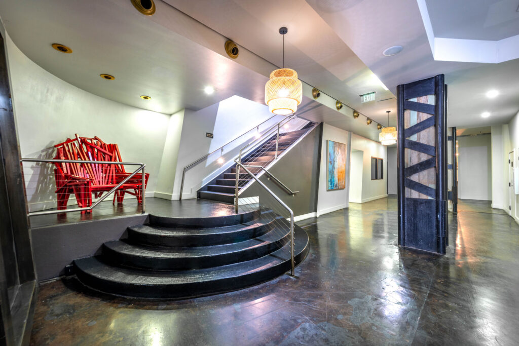 A curved black staircase leads to an upper level, with red chairs on a raised platform to the left and a framed painting on the wall.