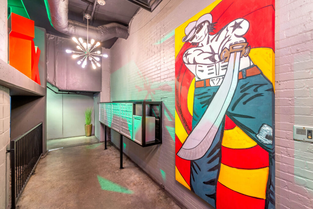 A hallway featuring a large mural of a manga-style character wielding a sword, with a wall-mounted bank of mailboxes and a decorative starburst chandelier nearby.