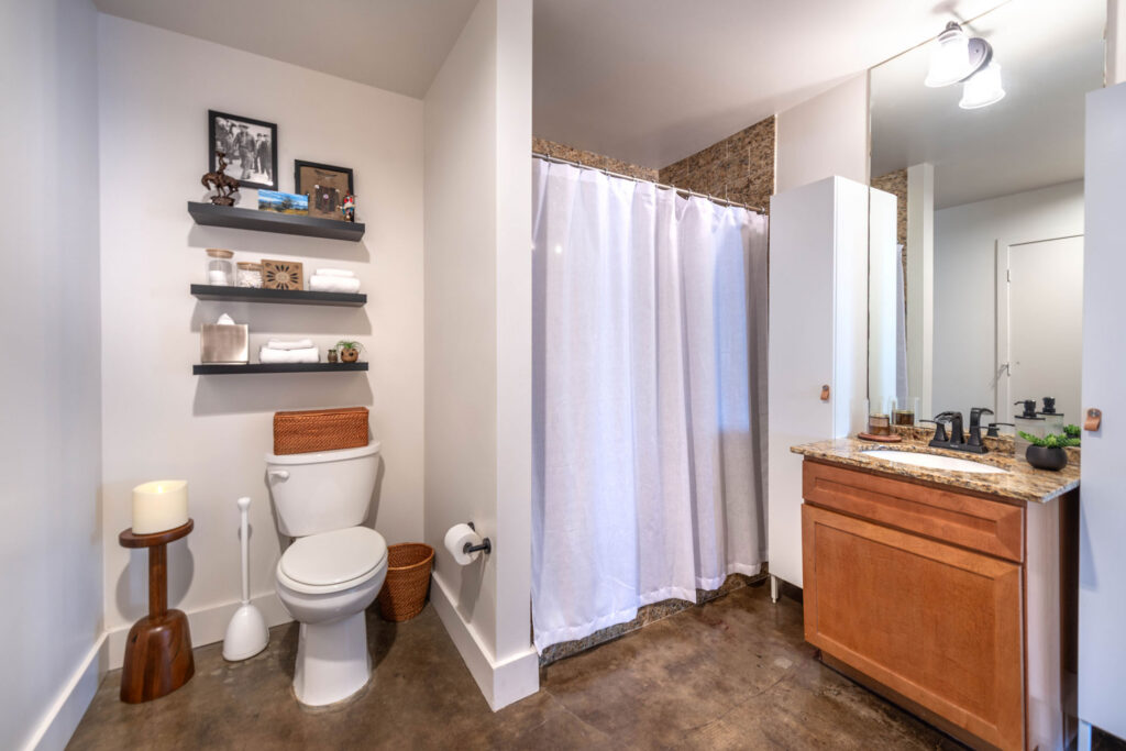 A bathroom with a white toilet, a shower with a white curtain, and a wood vanity with a stone countertop.