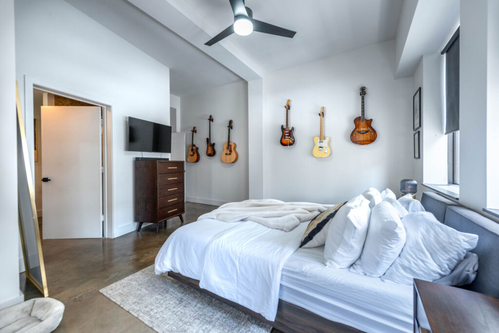 Bedroom with a bed, a dresser with a television, and six guitars mounted on the walls.
