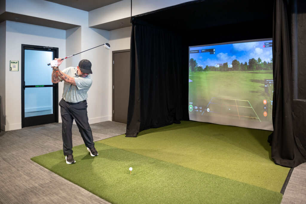 A man swinging a golf club in an indoor golf simulator studio.