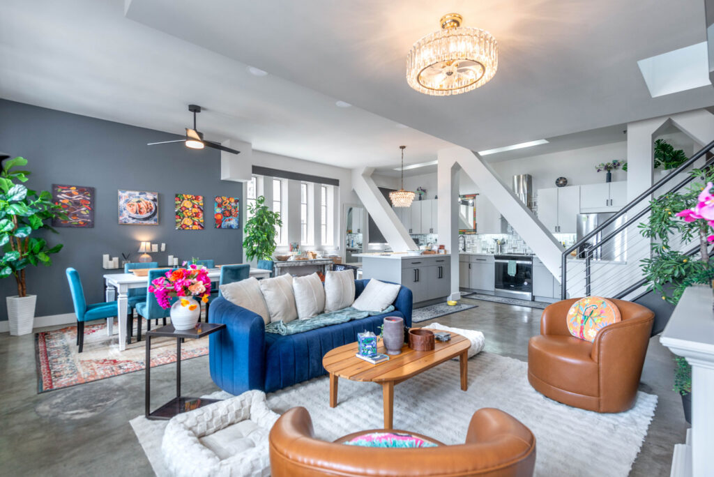 Open-plan living room with a blue sofa, two tan leather armchairs, a wooden coffee table, and a kitchen with grey cabinetry in the background.